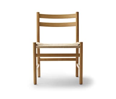 A minimalist dining chair crafted from natural oak wood, featuring an armless design with a gently curved, two-slat ladder backrest. The seat is hand-woven with natural paper cord, creating a textural contrast with the smooth wood frame. The chair stands on four round, tapered legs, with stretchers providing stability. — 3D model