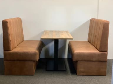 A set of two booth seats with a central table. The booth seats are upholstered in a brown, textured material and feature vertical tufting on the backrests. The table has a rectangular top made of wood planks and a black metal pedestal base. — 3D model
