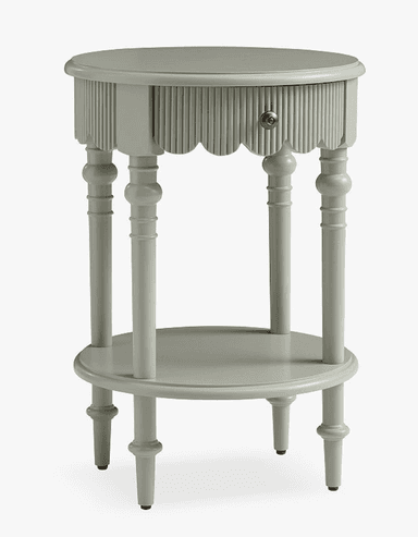 A light sage green, two-tiered accent table featuring a distinctive scalloped and reeded apron around the upper tabletop. The table is supported by four elegantly turned spindle legs, which also provide support for a circular lower shelf. The feet are simple and finished with small black glides. The overall design suggests a blend of traditional and cottage aesthetics. — 3D model