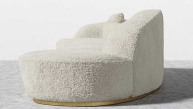 A contemporary, sculptural sofa featuring a deeply curved and organic silhouette, fully upholstered in a textured, cream-colored boucle fabric. The design includes integrated backrest elements that flow seamlessly from the main body. It is supported by a recessed, polished brass plinth base, giving it a floating appearance. — 3D model