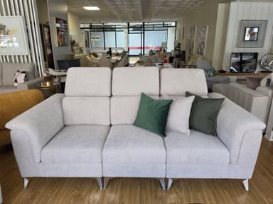 A modern light beige fabric sofa featuring three seat cushions, three backrests with individually adjustable headrests, and slim dark metal legs. It is accessorized with a mix of light green and dark green accent pillows. — 3D model