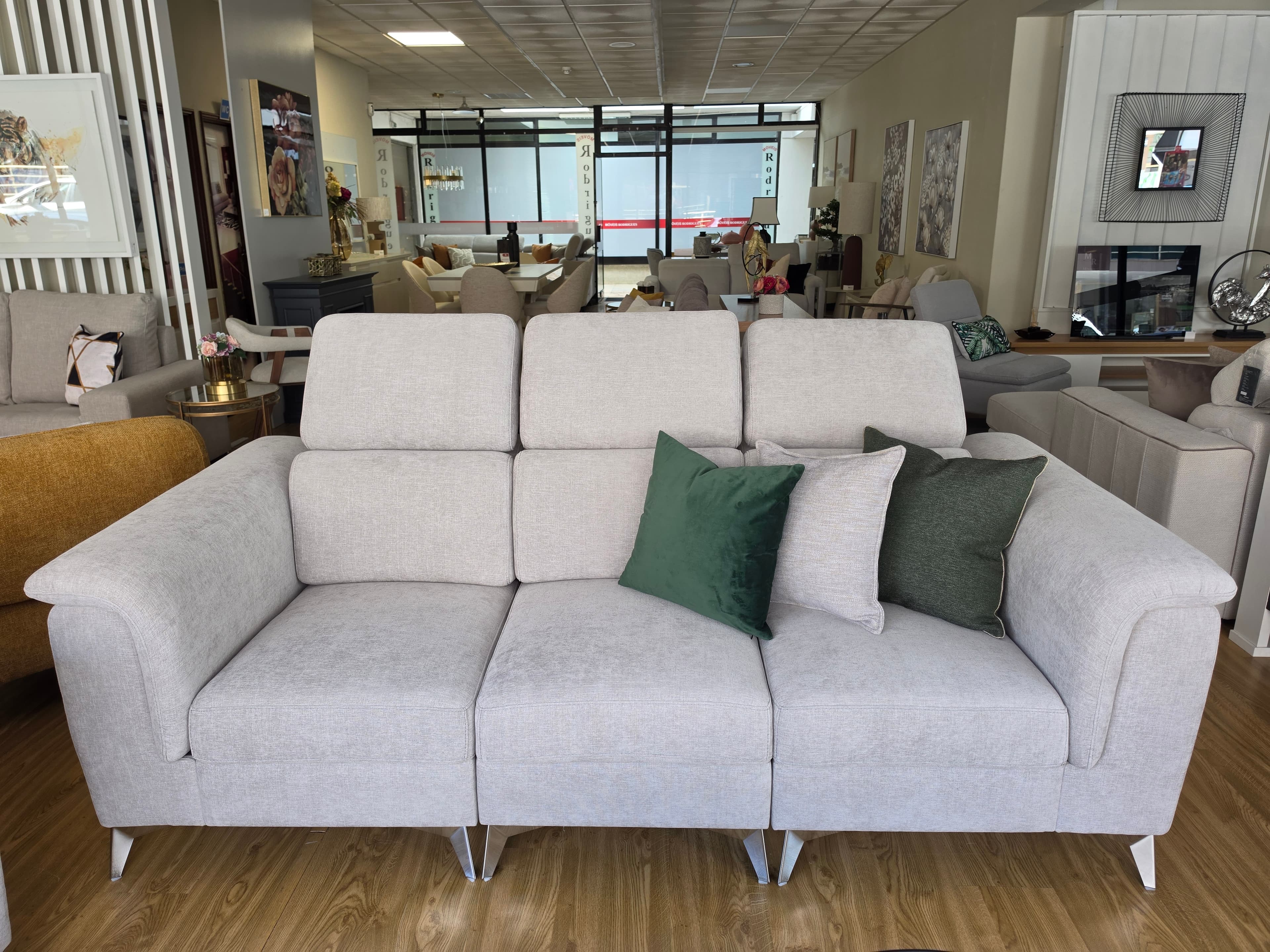 A modern light beige fabric sofa featuring three seat cushions, three backrests with individually adjustable headrests, and slim dark metal legs. It is accessorized with a mix of light green and dark green accent pillows. — 3D model