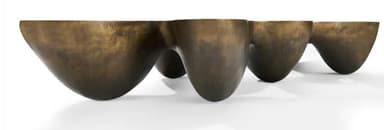 A low-profile, sculptural coffee table with an organic, undulating form and a patinated bronze finish. It features integrated depressions on its surface. — 3D model