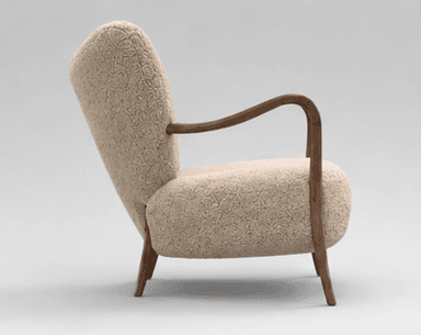 An armchair featuring a rounded, plush silhouette upholstered in a cream or beige bouclé fabric. It has visible, smoothly curved dark wooden armrests that extend downwards to form the front legs, and splayed wooden back legs. The backrest is slightly flared, providing a comfortable seating experience. — 3D model