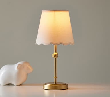 A small table lamp featuring a metallic brass-toned base and stem, supporting a conical linen fabric lampshade with a scalloped bottom edge. The stem includes a visible adjustment knob. — 3D model