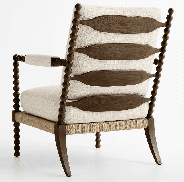 A lounge chair featuring a distinctive bobbin-turned dark wood frame, upholstered seat and back cushions in a light textured fabric, and decorative carved wooden back slats. — 3D model