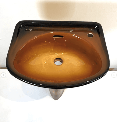 A contemporary pedestal sink featuring a striking ombré finish that transitions from dark black at the rim to a warm, glossy brown in the basin and down the pedestal. The basin has an elliptical shape with a single faucet hole and an integrated overflow slot. The pedestal base tapers elegantly from the basin to the floor, contributing to a sleek and modern aesthetic. — 3D model