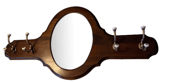A wall-mounted decorative wooden panel featuring an oval mirror in the center and multiple brass coat hooks with white ceramic knobs on either side. The dark-finished wood frame has carved details along its edges. — 3D model