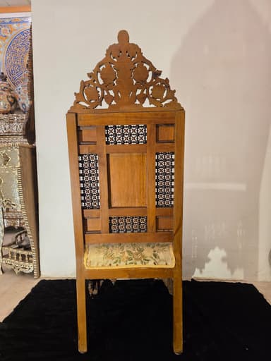 A highly ornate accent chair featuring intricate marquetry and inlay work. The chair has a tall, elaborately carved back with floral motifs and geometric patterns. The seat is upholstered in a light-colored fabric with a floral pattern. The base of the chair, including the legs and the area beneath the seat, is constructed from dark wood and heavily decorated with mother-of-pearl inlay, creating floral and geometric designs. The legs have an arched structure. The overall construction suggests a piece of antique or artisan craftsmanship. — 3D model