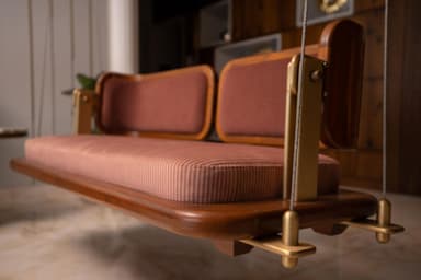 A modern two-seater swing seat featuring a curved wooden frame, upholstered cushions, and suspended by metal cables. — 3D model