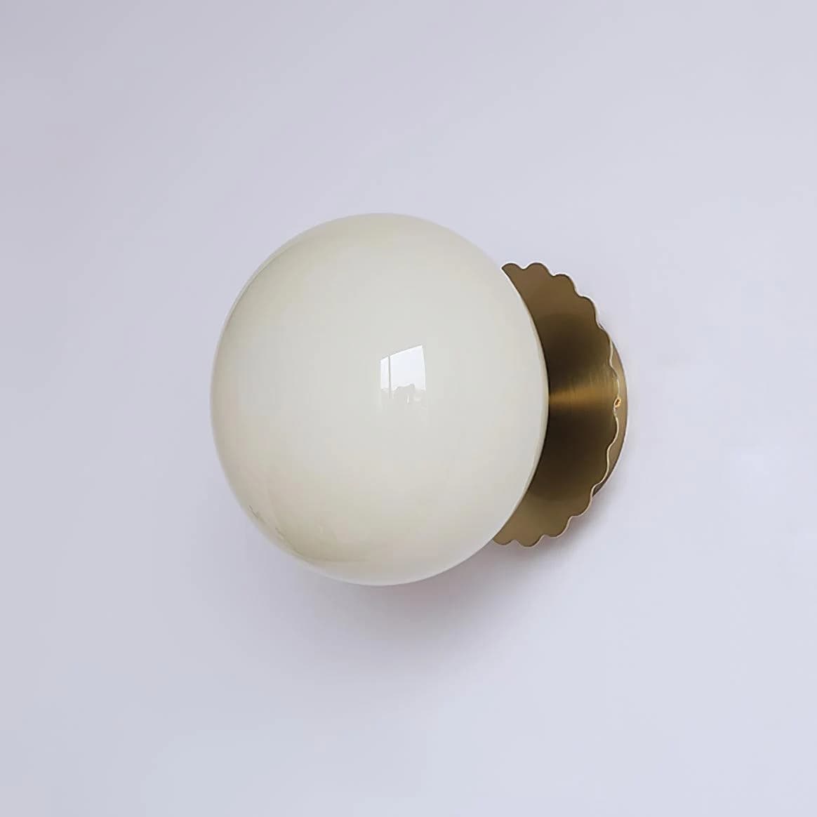 A modern wall-mounted light fixture featuring a spherical opal glass globe diffuser and a scalloped brass mounting plate. — 3D model