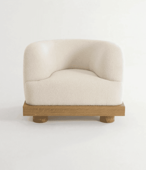 A contemporary armchair with a rounded, upholstered seat and back, supported by a distinct wooden base and legs. The upholstery has a textured, boucle-like finish. The base is rectangular with a prominent grain, and it rests on four cylindrical legs. — 3D model