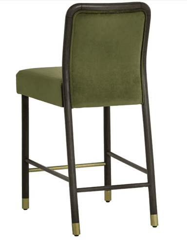 A contemporary bar stool featuring olive green velvet upholstery on both the seat and a rounded backrest. The frame is constructed from dark-stained wood, possibly black oak, with a distinctive curved detail around the backrest. The four tapered legs are also dark wood and are reinforced by stretchers, including a prominent brass-finished footrest. Each leg is capped with a subtle brass ferrule. — 3D model
