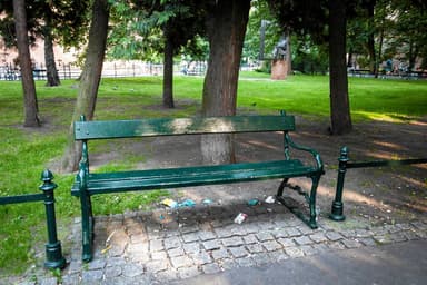 A traditional outdoor bench featuring a dark green finish, composed of parallel wooden slats for the seat and backrest, supported by decorative cast metal end frames with scrollwork armrests. — 3D model