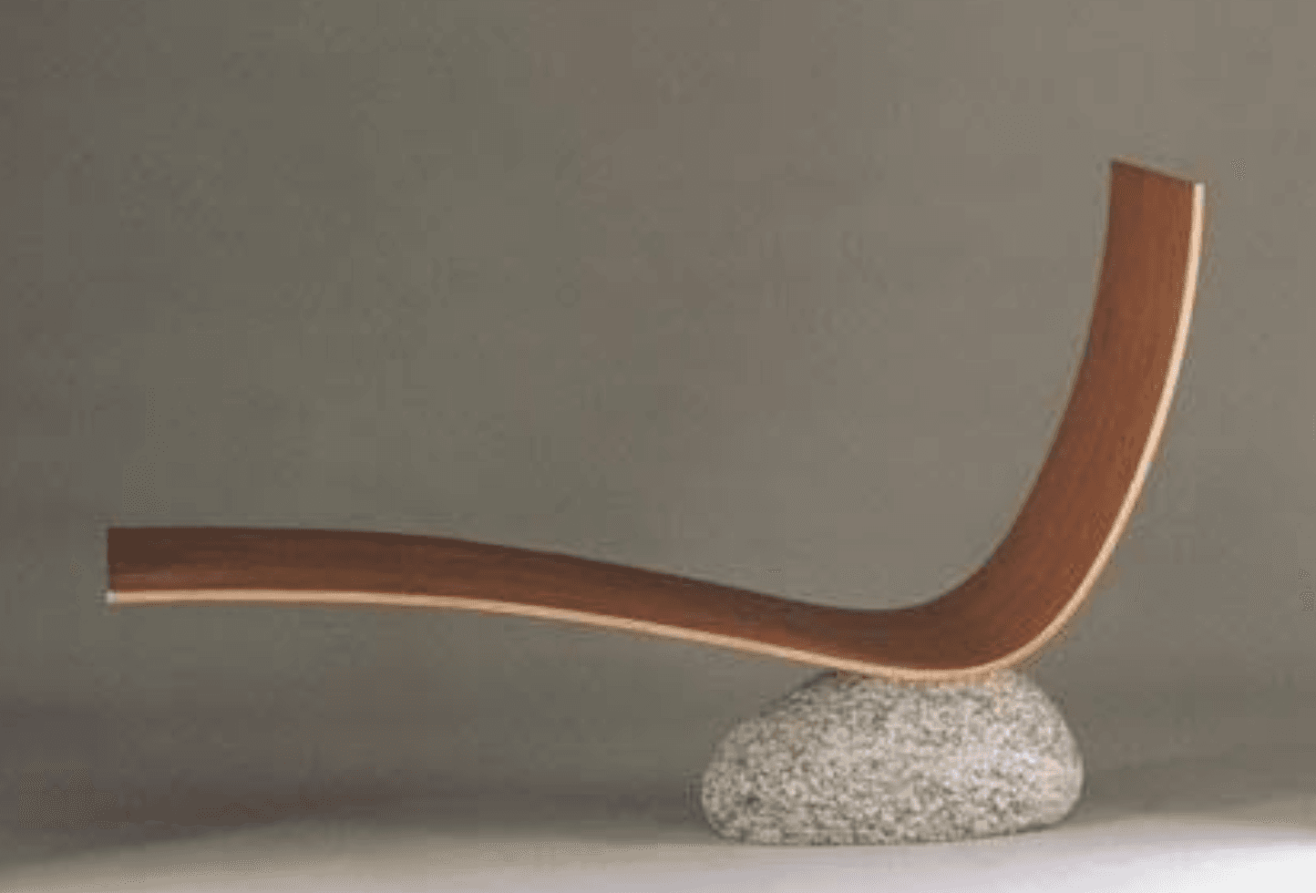 A modern sculptural chaise lounge featuring a gracefully curved, laminated wooden form supported by a single, large, irregularly shaped natural stone base. The wood has a light brown, natural grain finish, and the stone is speckled grey, creating a striking contrast of organic materials and minimalist design. — 3D model