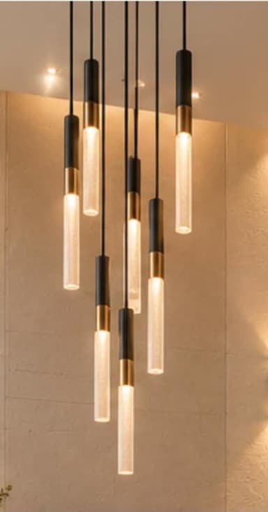 A modern multi-light pendant chandelier featuring nine individual cylindrical light sources suspended from a circular black canopy. Each light comprises a black cylindrical top, a brass band, and a frosted white or textured glass lower section that emits light. The lights hang at varying lengths, creating a dynamic, clustered arrangement. — 3D model