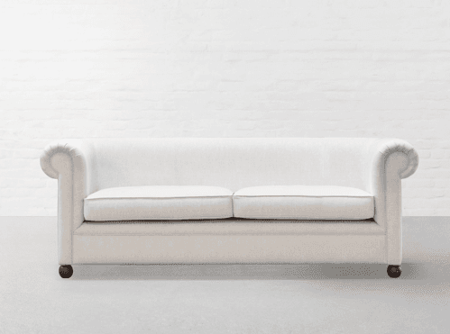 A cream-colored, two-seater loveseat featuring a traditional design with gracefully rolled arms and an upholstered back. It has two separate loose seat cushions, each with subtle piping along the edges, and rests on short, dark-colored turned legs. — 3D model