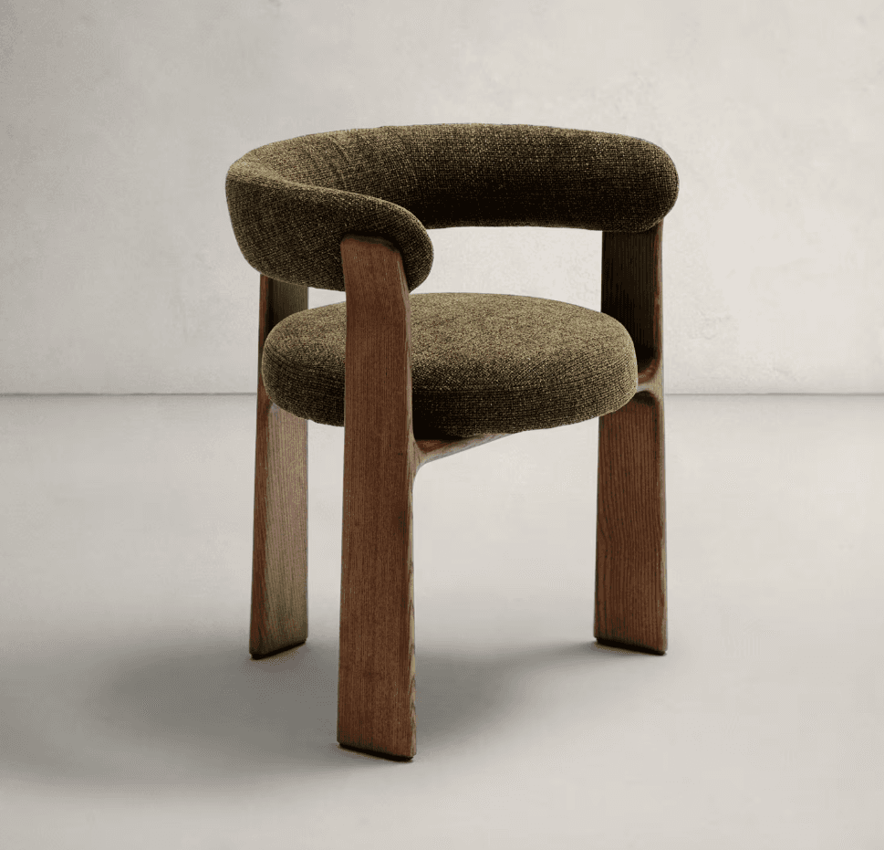 A modern accent chair featuring a curved, upholstered backrest that wraps around to form armrests. The seat is also upholstered. The chair has a solid wooden base and legs with a distinctive, sculptural design. — 3D model