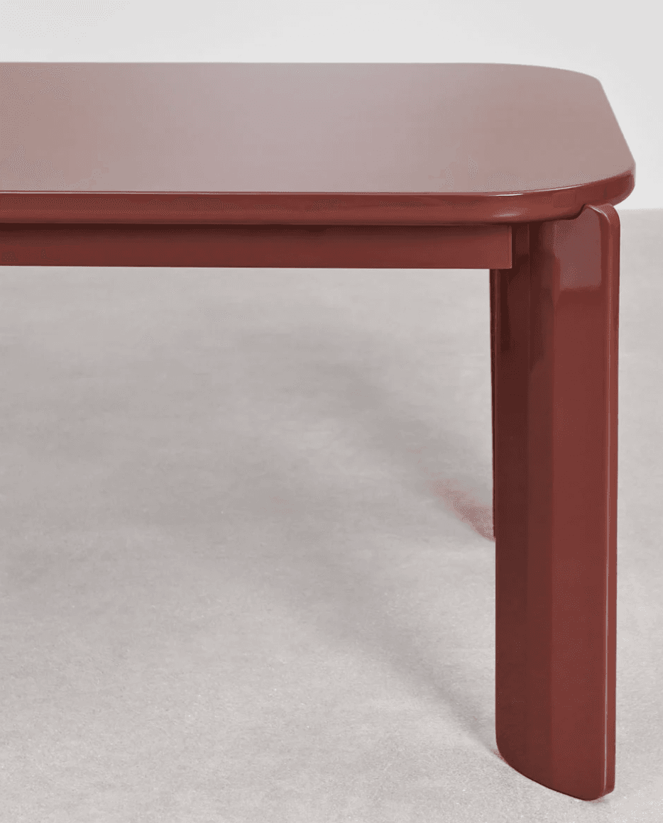 A close-up view of a table's corner and one leg. The table has a rectangular top with rounded corners and a thick, slightly beveled edge. The leg is solid and rectangular in cross-section, with a subtle taper towards the bottom and a rounded end. The design appears modern and minimalist. — 3D model