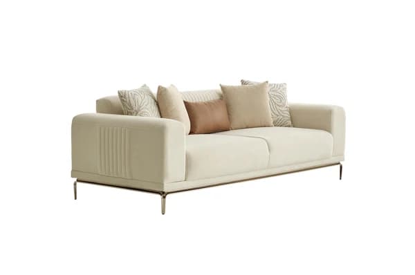 A contemporary three-seater sofa upholstered in a light cream-colored fabric, featuring wide, squared arms with vertical pleating on the outer sides. The sofa rests on a minimalist metal base with slender, angled legs, giving it a modern appearance. It includes loose seat cushions and multiple decorative throw pillows in coordinating neutral tones and patterns. — 3D model
