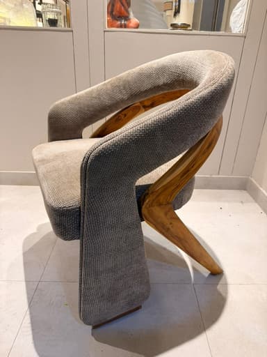 A contemporary armchair with a curved backrest and upholstered seat and arms. The frame appears to be constructed from wood, visible as a curved piece supporting the backrest. The upholstery is a textured fabric in a neutral tone. — 3D model