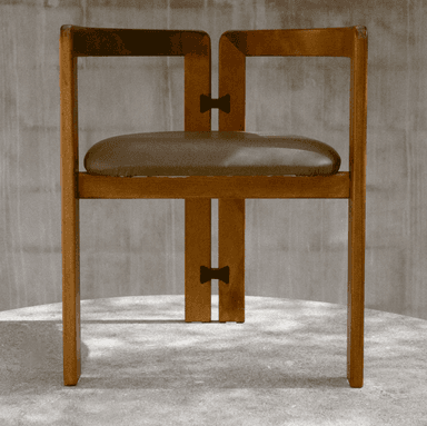 A wooden chair with a cushioned seat and a distinct 'butterfly' joint connecting the vertical support beams. The chair has a minimalist design with clean lines, featuring four legs, a seat, and a backrest composed of two vertical posts connected by a horizontal element near the top. The wood appears to be a medium-toned hardwood. — 3D model