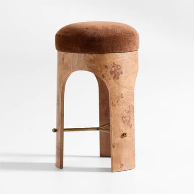 A stool with a rounded, upholstered seat and a pedestal base. The base is constructed from a wood veneer with a distinctive burl pattern, featuring an arched opening and supporting a subtle cross-brace. A small brass-colored knob is visible on each side of the base. — 3D model