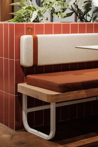 A modern bench featuring a light-toned wooden seat platform, a padded brown leather cushion for the seat, and a separate, rectangular off-white fabric backrest cushion. The backrest is secured to the main structure by two light brown leather straps with metal hardware. The bench is supported by two minimalist U-shaped white metal legs. — 3D model