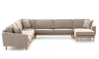 A modern L-shaped sectional sofa upholstered in a light beige or taupe fabric, featuring a right-hand facing chaise lounge. The sofa has a low-profile design with clean lines, track arms, and exposed wooden legs. Each cushion features piped edge detailing, and multiple throw pillows are included. — 3D model