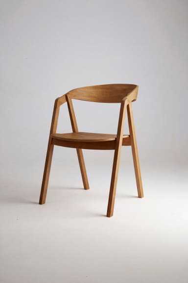 A modern armchair constructed from light-toned wood, featuring a curved backrest that flows into integrated armrests. The seat is an upholstered pad covered in a light grey textured fabric. — 3D model