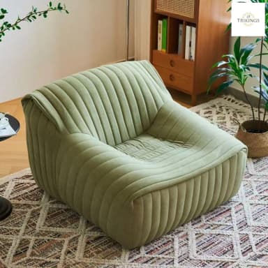A fully upholstered lounge chair featuring vertical channel tufting across its entire surface. The chair has a low profile, a deep seat, and integrated armrests that seamlessly curve upwards from the seat to form the backrest. The design is minimalist and contemporary, emphasizing comfort and a soft, inviting aesthetic. The upholstery appears to be a plush fabric, likely velvet or a similar material, in a muted sage green color. — 3D model