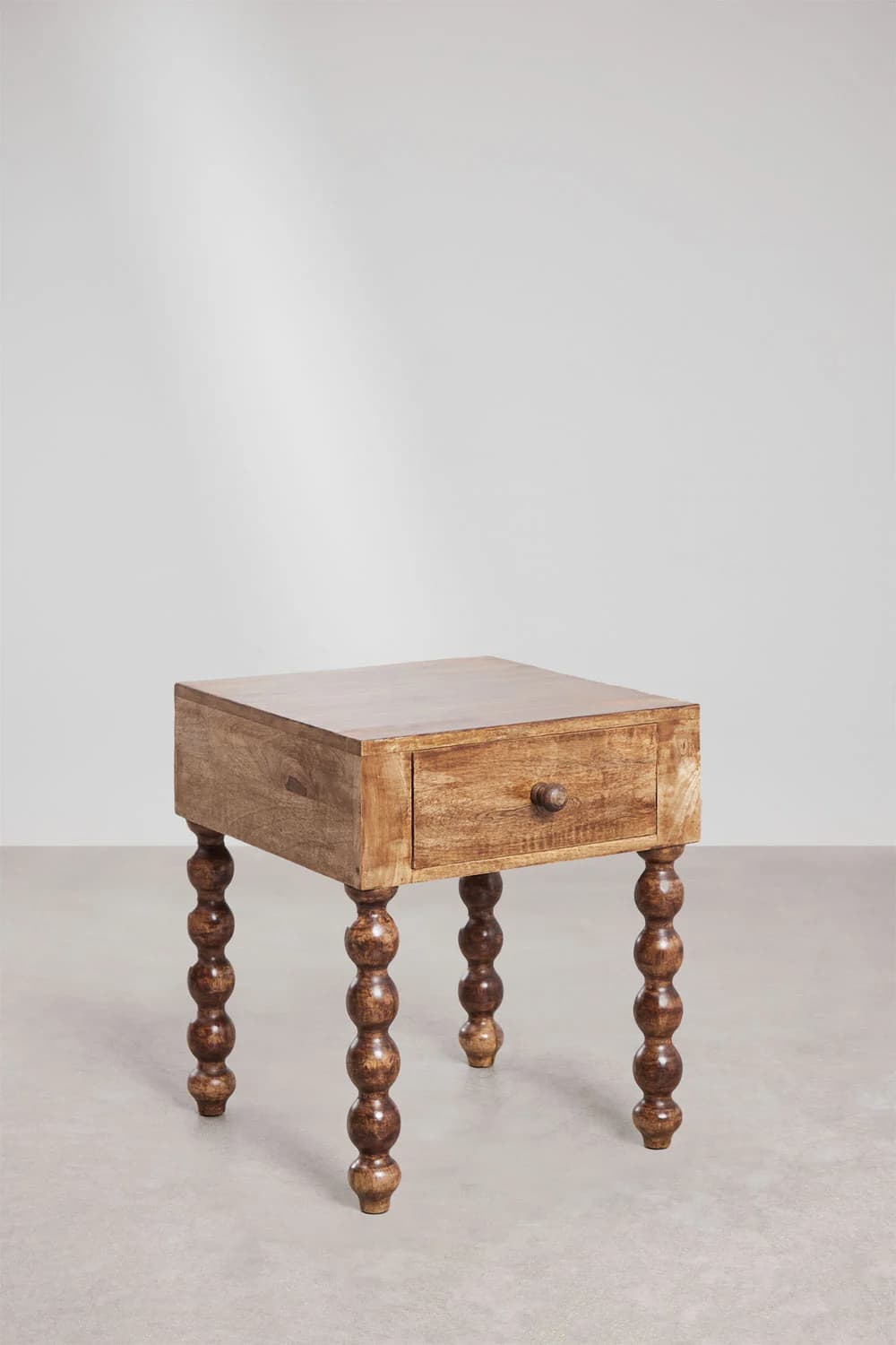 A wooden end table with a single drawer and decorative turned legs. The table has a rectangular top and a body constructed from wood planks. It features a single drawer with a round wooden knob. The legs are a prominent design element, characterized by a series of stacked, rounded turnings resembling beads or bobs. — 3D model