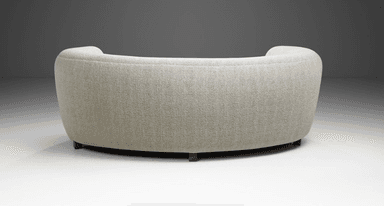 A curved, fully upholstered sofa featuring a serpentine form, rounded back and integrated armrests, and short, tapered wooden legs. It is covered in a light-colored, textured woven fabric. — 3D model