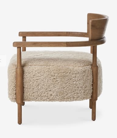 A contemporary armchair featuring a light brown wooden frame and a plush, light beige boucle or sherpa upholstered seat and backrest. The frame includes integrated armrests and subtly shaped legs. The backrest is a curved wooden panel. — 3D model