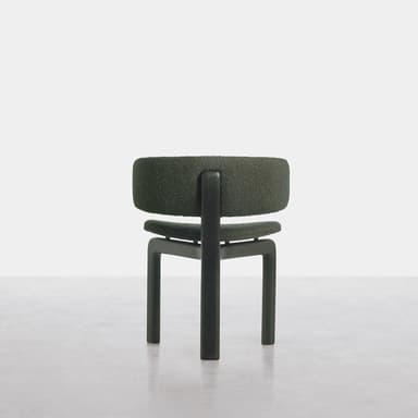A modern armless chair featuring a low, plush, dark green bouclé-textured upholstered backrest and seat, separated by a distinct gap. The chair is supported by a sturdy, dark, minimalist H-shaped frame that also forms its four block-like legs. The design emphasizes clean lines and a compact footprint. — 3D model