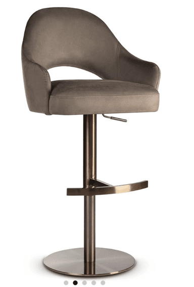 A contemporary bar stool featuring a taupe or light gray upholstered seat and back with integrated armrests and a distinctive cutout design. It stands on a bronze-finished metal pedestal base with a circular footrest and includes a lever for height adjustment. — 3D model