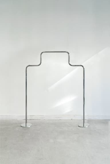 A minimalist, freestanding garment rack made of polished chrome or silver-toned metal, featuring a curved upper bar for hanging items and two vertical supports with flat circular bases. — 3D model