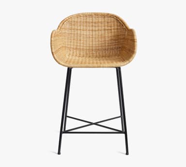 A bar stool featuring a natural woven rattan seat and backrest with integrated armrests, supported by a minimalist black metal frame with an X-shaped footrest. — 3D model
