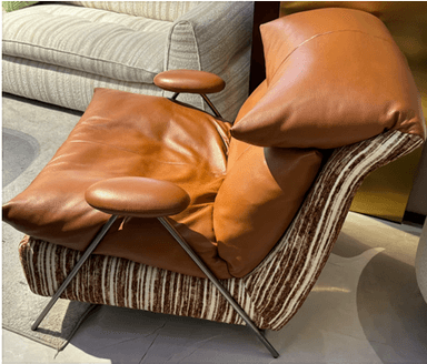 A contemporary lounge chair featuring a distinctive two-material upholstery design. The plush, tufted seat and back cushions are upholstered in smooth brown leather, providing comfort and a sophisticated look. The main body and frame are covered in a textured, multi-toned striped fabric, creating a contrasting visual interest. The chair is supported by sleek, angled metal legs and has small, rounded, padded armrests. — 3D model