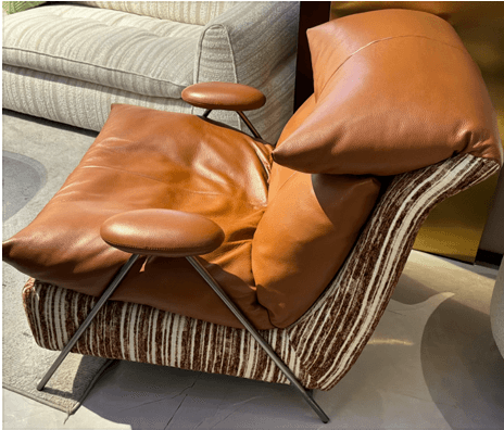 A contemporary lounge chair featuring a distinctive two-material upholstery design. The plush, tufted seat and back cushions are upholstered in smooth brown leather, providing comfort and a sophisticated look. The main body and frame are covered in a textured, multi-toned striped fabric, creating a contrasting visual interest. The chair is supported by sleek, angled metal legs and has small, rounded, padded armrests. — 3D model