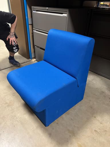 A single-seat armchair upholstered in a textured blue fabric. The armchair features a low profile with a cushioned seat and a straight, upright backrest. It appears to have a boxed base with small, dark feet. — 3D model