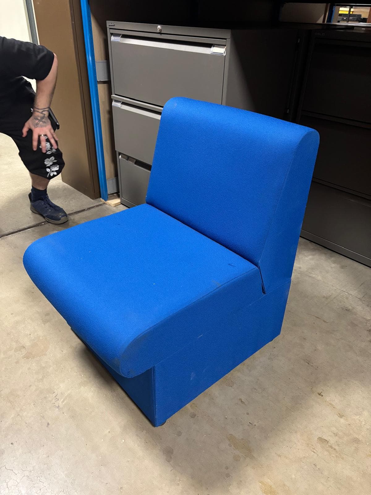 A single-seat armchair upholstered in a textured blue fabric. The armchair features a low profile with a cushioned seat and a straight, upright backrest. It appears to have a boxed base with small, dark feet. — 3D model