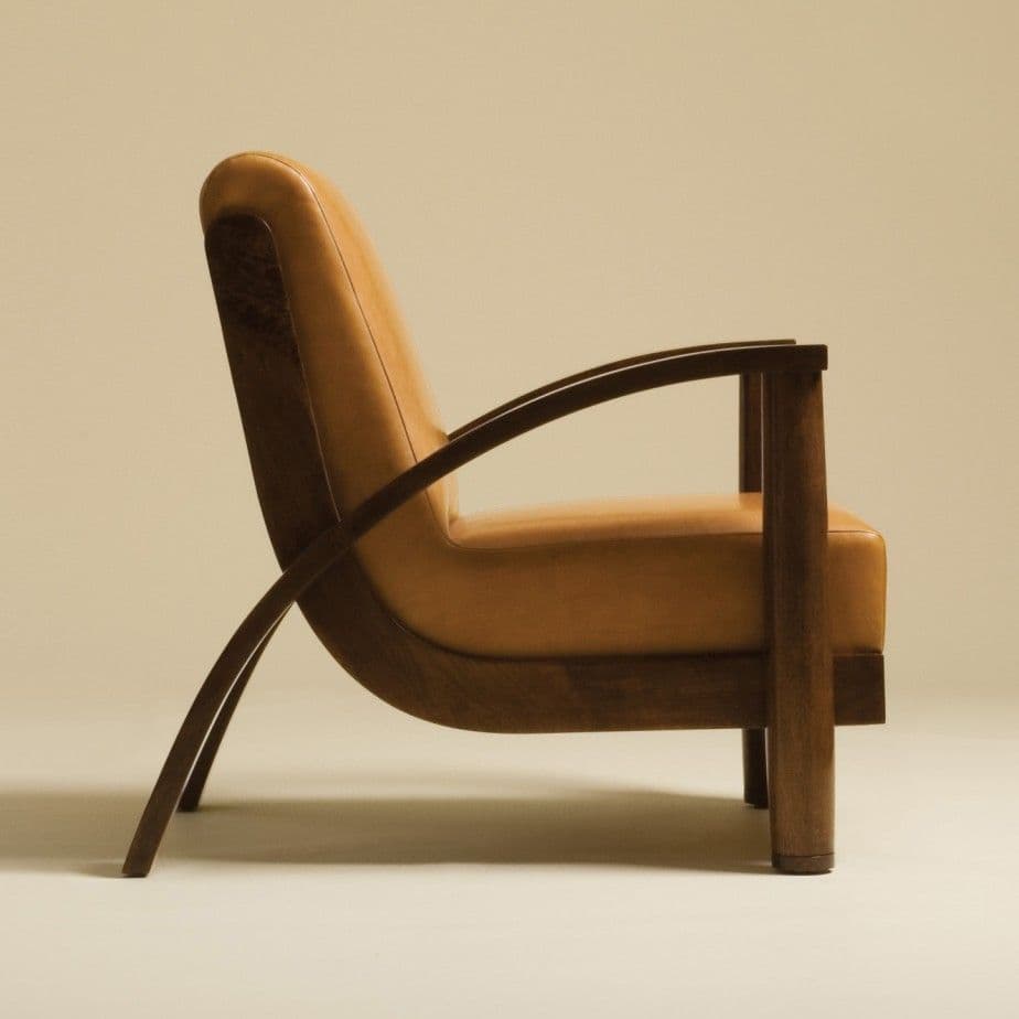An armchair with a curved wooden frame and a padded, upholstered seat and back. The armchair features a high backrest that gently curves forward, and armrests formed by a smooth wooden arc supported by vertical wooden legs. The upholstery appears to be a warm, tan-colored fabric. — 3D model