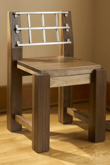 A modern wooden chair with a distinctive metal backrest. The chair features a solid wood seat and legs, with a back composed of vertical wooden uprights supporting a horizontal grid of metal bars. The construction appears sturdy and the design emphasizes geometric shapes. — 3D model
