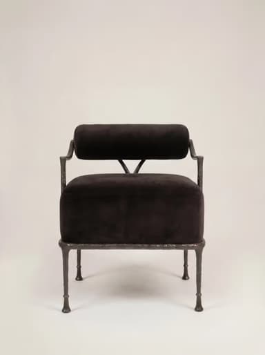 A robust armchair featuring a dark, possibly black or very dark brown, velvet upholstered seat and a cylindrical backrest. The frame is constructed from dark, textured, possibly forged iron or a similar heavy metal, exhibiting a somewhat raw and organic aesthetic. The legs are slender but robust, tapering slightly to small, disc-like feet. The backrest is suspended above the seat, supported by the frame's uprights, with a small V-shaped support element visible at the rear. — 3D model