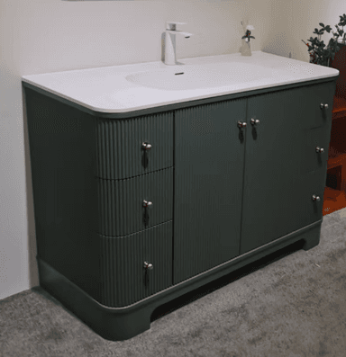 A modern dark green bathroom vanity featuring a fluted cabinet design, an integrated white ceramic sink, and brass-finished hardware. It includes both cabinet storage and drawers, sitting on a solid base. — 3D model