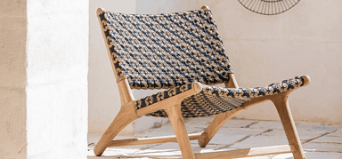 A modern, low-slung armless lounge chair featuring a sturdy teak wood frame and an intricately woven seat and backrest. The weaving combines black and natural-colored fibers in a geometric pattern, providing both support and a distinctive aesthetic. The frame has a natural wood finish, and the chair exhibits a relaxed, reclined posture. — 3D model