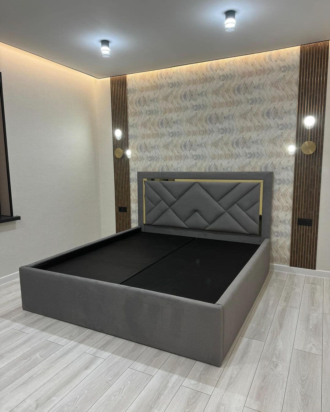 A contemporary platform bed frame featuring full gray fabric upholstery. The prominent headboard showcases a distinctive geometric quilted pattern in the same gray fabric, framed by a lustrous gold-finished metal trim. The low-profile bed base is also upholstered, providing a clean and integrated look, designed to support a mattress directly without the need for a box spring. — 3D model