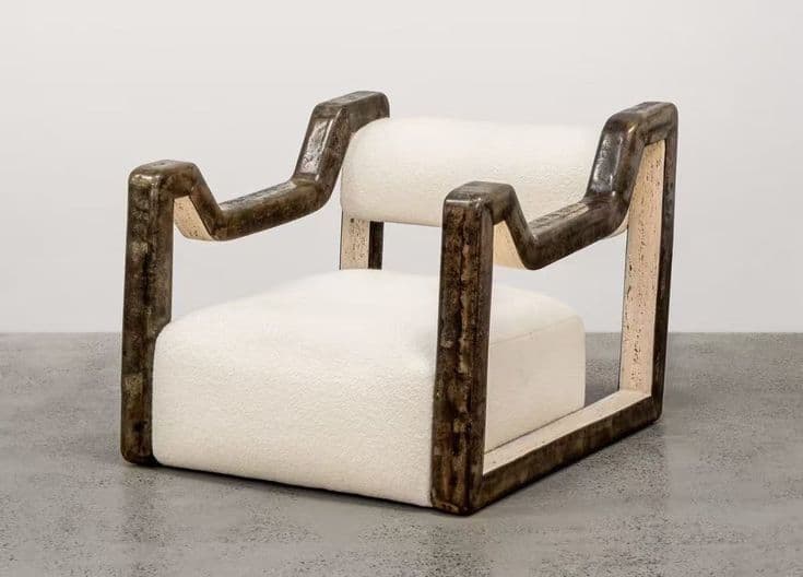 A contemporary armchair featuring a distinct sculptural frame and upholstered seat and back. The frame has a dark, textured, possibly metallic or resin finish with visible striations and color variations. The seat and back cushions are upholstered in a thick, looped, off-white fabric, likely bouclé or a similar textured textile. The overall design is angular and bold, with the armrests extending from the frame in a striking, curved, and angular manner. — 3D model