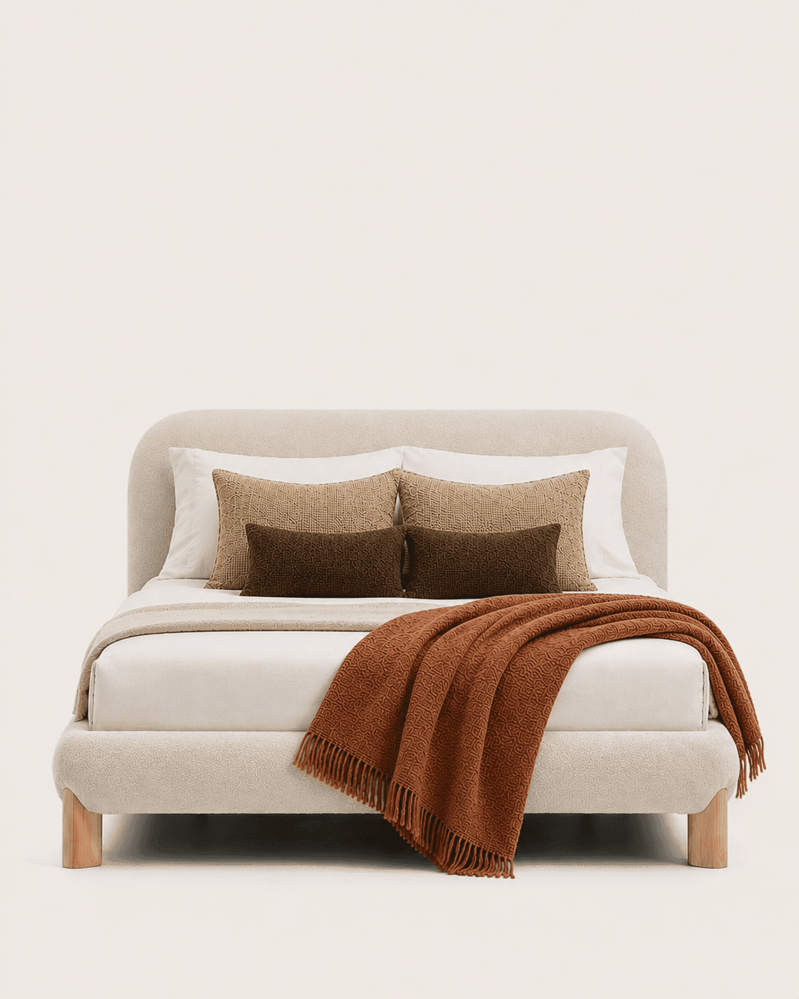 An upholstered platform bed featuring a soft, cream-colored, textured fabric. The bed includes an integrated headboard and footboard with rounded edges, creating a contemporary and organic aesthetic. It stands on four short, cylindrical light wood legs, elevating the frame slightly off the ground. The bed is dressed with white bedding, an off-white textured throw, and several decorative pillows in shades of brown and terracotta, along with a rust-colored knitted blanket draped over the foot of the bed. — 3D model